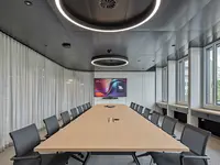 Büro- und Gemeinflächenausbau Georg Fischer AG in Schaffhausen: Der grosszügige Konferenzraum greift mit gerundeter Raumführung, umlaufendem Vorhang und kreisförmigen Leuchten die fliessende Formensprache des gesamten Innenausbaus auf. Eine ruhige, repräsentative Atmosphäre für Besprechungen und Austausch.