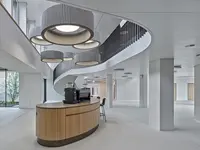 Büro- und Gemeinflächenausbau Georg Fischer AG in Schaffhausen: Fliessende Formen prägen den offenen Begegnungsbereich und setzen sich vom geschwungenen Café-Tresen bis zur markanten Treppenanlage fort. Die skulpturale Beleuchtung und die reduzierte Materialisierung verleihen der Gemeinfläche einen repräsentativen, beinahe organischen Charakter.