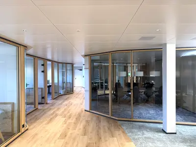 Umbau Verwaltungsgebäude in Pfäffikon: Gebogene Holz-Glas-Trennwände aus gebürsteter Eiche folgen der Raumgeometrie und schaffen transparente Besprechungsräume mit einer fliessenden, eleganten Linienführung.