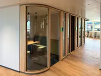 Umbau Verwaltungsgebäude in Pfäffikon: Präzise ausgeführte Glasradien und Rahmen aus gebürsteter Eiche formen eine fliessende Holz-Glas-Trennwand mit warmer, hochwertiger Anmutung.
