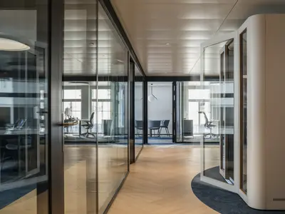 Elegante Doppelverglasung mit raumhohen Ganzglaswänden verbindet transparente Büroarchitektur mit hohem Schallschutz. Die filigranen schwarzen Profile strukturieren die Arbeits- und Besprechungsräume und erhalten gleichzeitig das offene, lichtdurchflutete Raumgefühl.