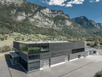 Neubau und Erweiterung Industriehalle Stoss in Walenstadt: Klare Linien, grosszügige Glasflächen und eine rhythmisch gegliederte Fassade prägen den modernen Industriebau und fügen ihn markant in die alpine Umgebung ein.