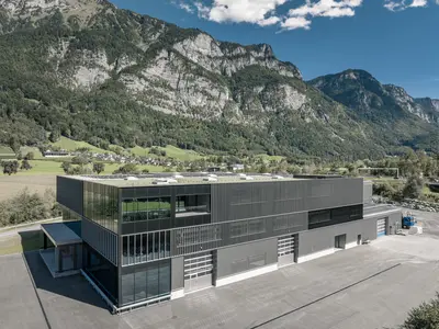 Neubau und Erweiterung Industriehalle Stoss in Walenstadt: Klare Linien, grosszügige Glasflächen und eine rhythmisch gegliederte Fassade prägen den modernen Industriebau und fügen ihn markant in die alpine Umgebung ein.