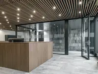 Neubau und Erweiterung Industriehalle Stoss in Walenstadt: Grossflächige Einscheibenverglasung schafft transparente Raumgrenzen und verbindet den Empfang mit der angrenzenden Architektur. Schwarze Profile setzen einen präzisen Kontrast zu Holz und Naturstein.