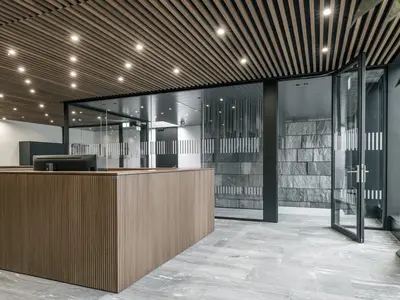 Neubau und Erweiterung Industriehalle Stoss in Walenstadt: Grossflächige Einscheibenverglasung schafft transparente Raumgrenzen und verbindet den Empfang mit der angrenzenden Architektur. Schwarze Profile setzen einen präzisen Kontrast zu Holz und Naturstein.