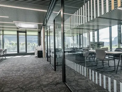 Neubau und Erweiterung Industriehalle Stoss in Walenstadt: Grossflächige Einscheibenverglasungen gliedern die Arbeitsbereiche transparent und lassen Licht und Sichtachsen durch die Büroflächen fliessen. Schwarze Profile und dezente Sichtschutzmarkierungen unterstreichen die klare, moderne Architektur.